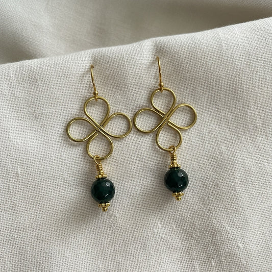 Blakeley Lane Jewelry gold wire clover drop earrings with faceted deep green beads on a white linen background.