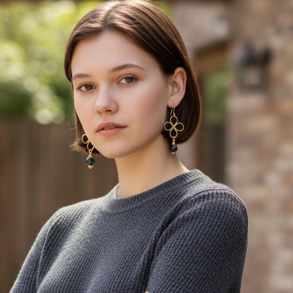 Blakeley Lane Jewelry gold wire clover drop earrings with faceted green beads worn by a woman in a grey sweater.
