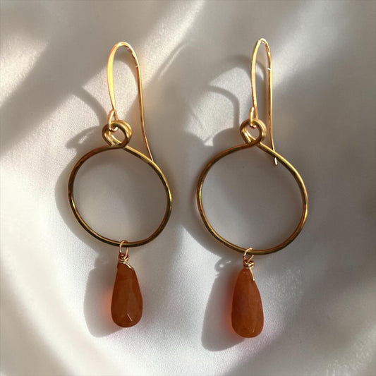 Blakeley Lane Jewelry gold-tone hoop earrings with faceted amber teardrop gemstones on a white silk background.