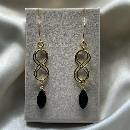 Blakeley Lane Jewelry gold-tone infinity drop earrings with marquise-cut black stones on a white display stand.