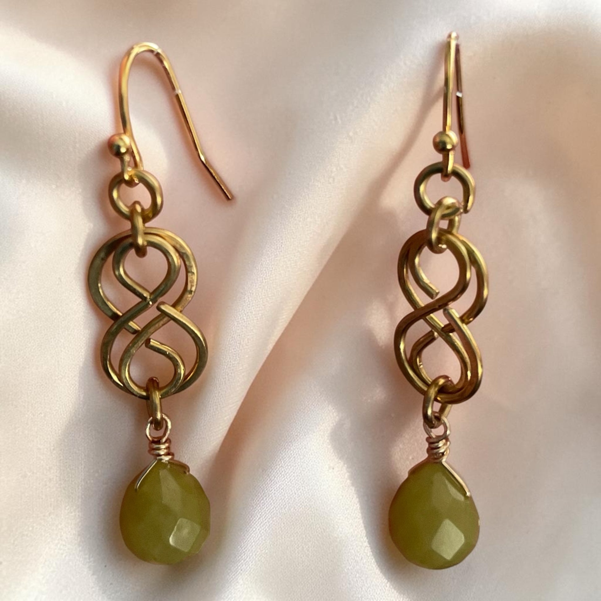 Blakeley Lane Jewelry gold-toned infinity drop earrings with faceted olive-green gemstone pendants on hook backings.