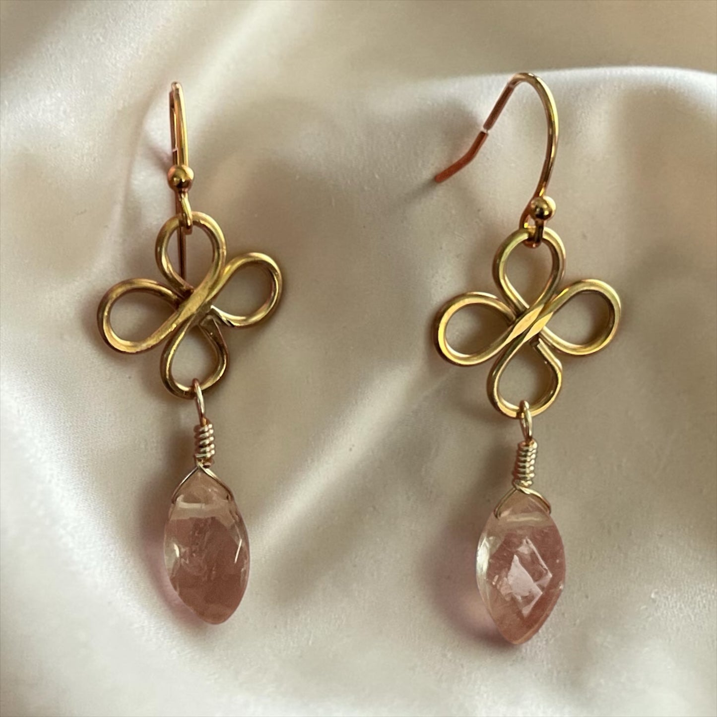 Blakeley Lane Jewelry gold-tone wire-wrapped clover earrings with faceted pink crystal drops on a white silk background