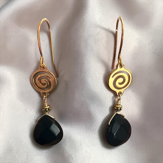Blakeley Lane Jewelry gold-tone spiral drop earrings with faceted black teardrop stones on a white silk background.