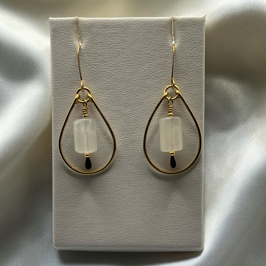 Blakeley Lane Jewelry gold teardrop dangle earrings with milky stone beads and dark accent drops on a display stand.