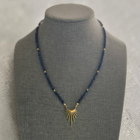 Blakeley Lane Jewelry navy beaded necklace with a gold-tone sunburst pendant on a grey display bust