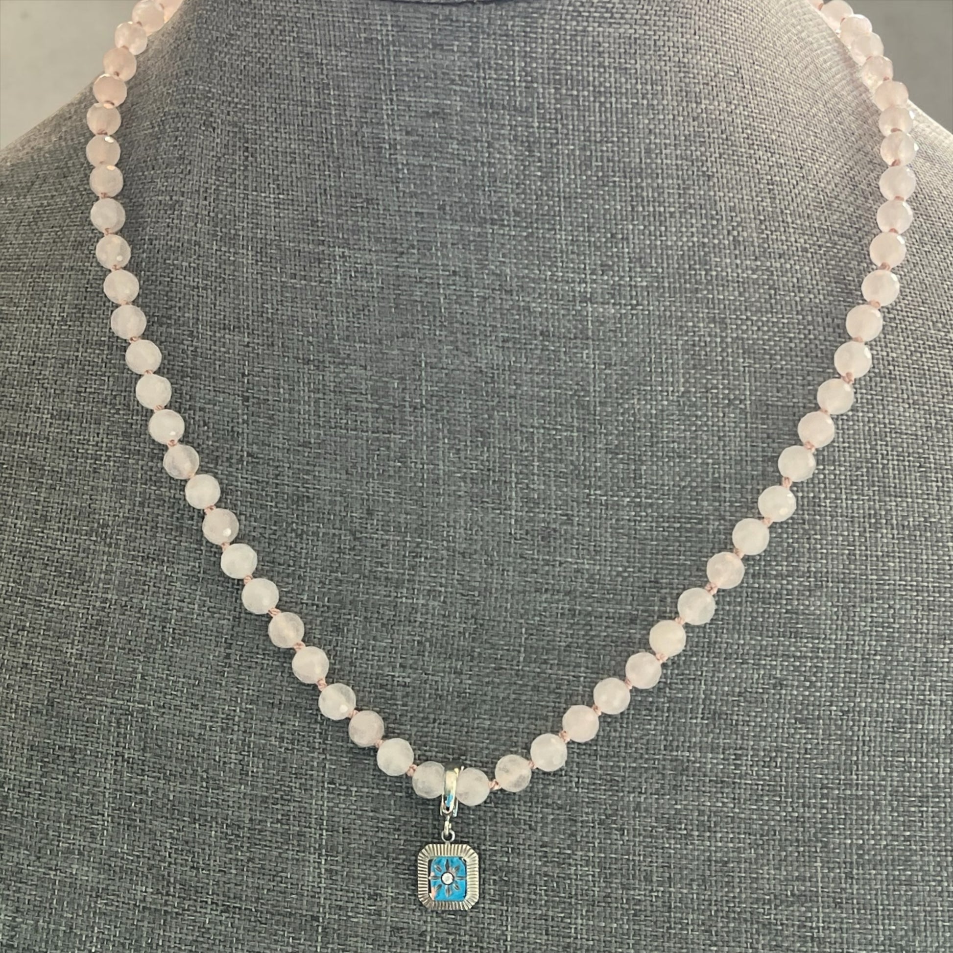 Blakeley Lane Jewelry rose quartz beaded necklace with a rectangular blue enamel and silver pendant on a grey bust.