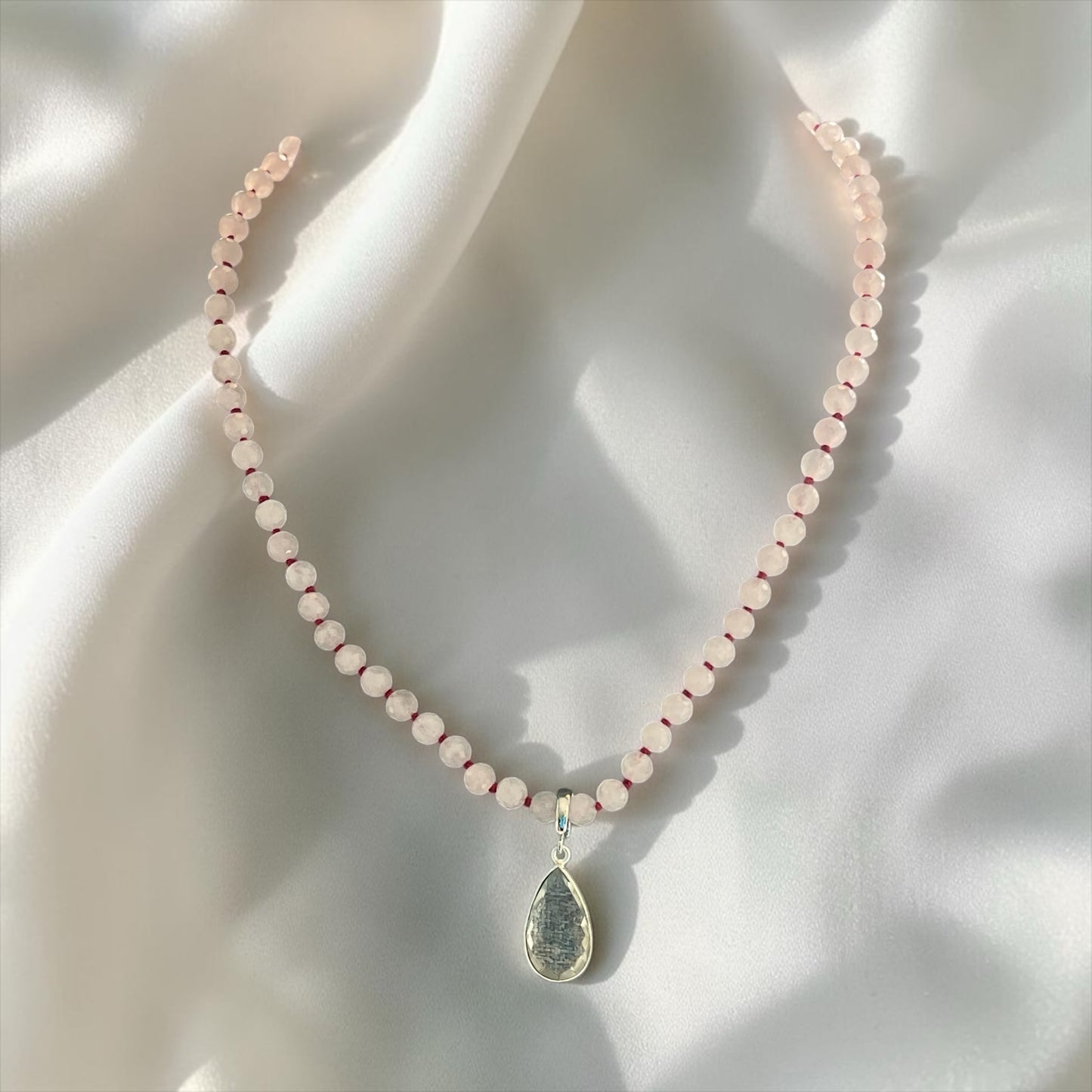 Blakeley Lane Jewelry beaded necklace with faceted rose quartz beads and a metallic teardrop pendant on white silk.