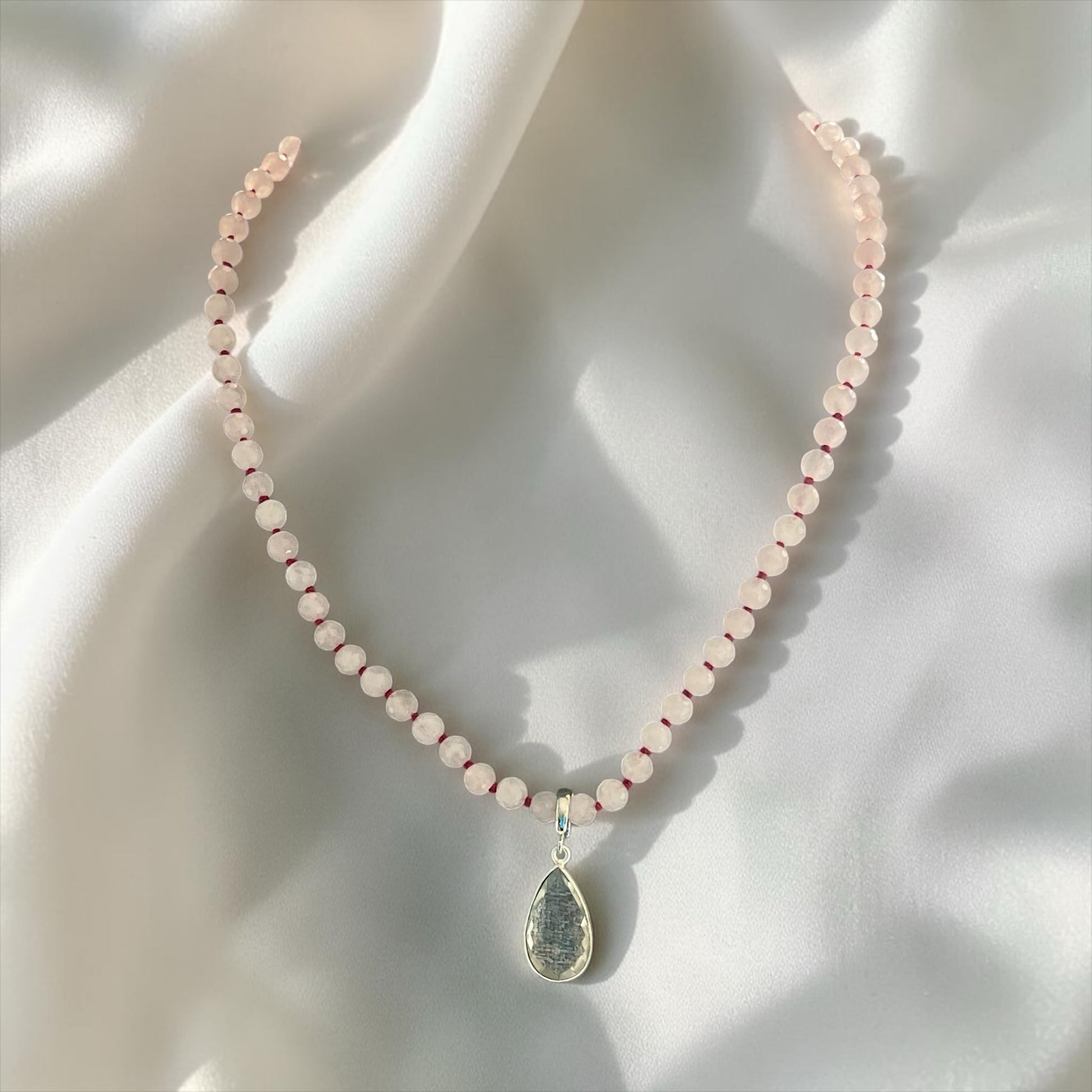Blakeley Lane Jewelry beaded necklace with faceted rose quartz beads and a metallic teardrop pendant on white silk.