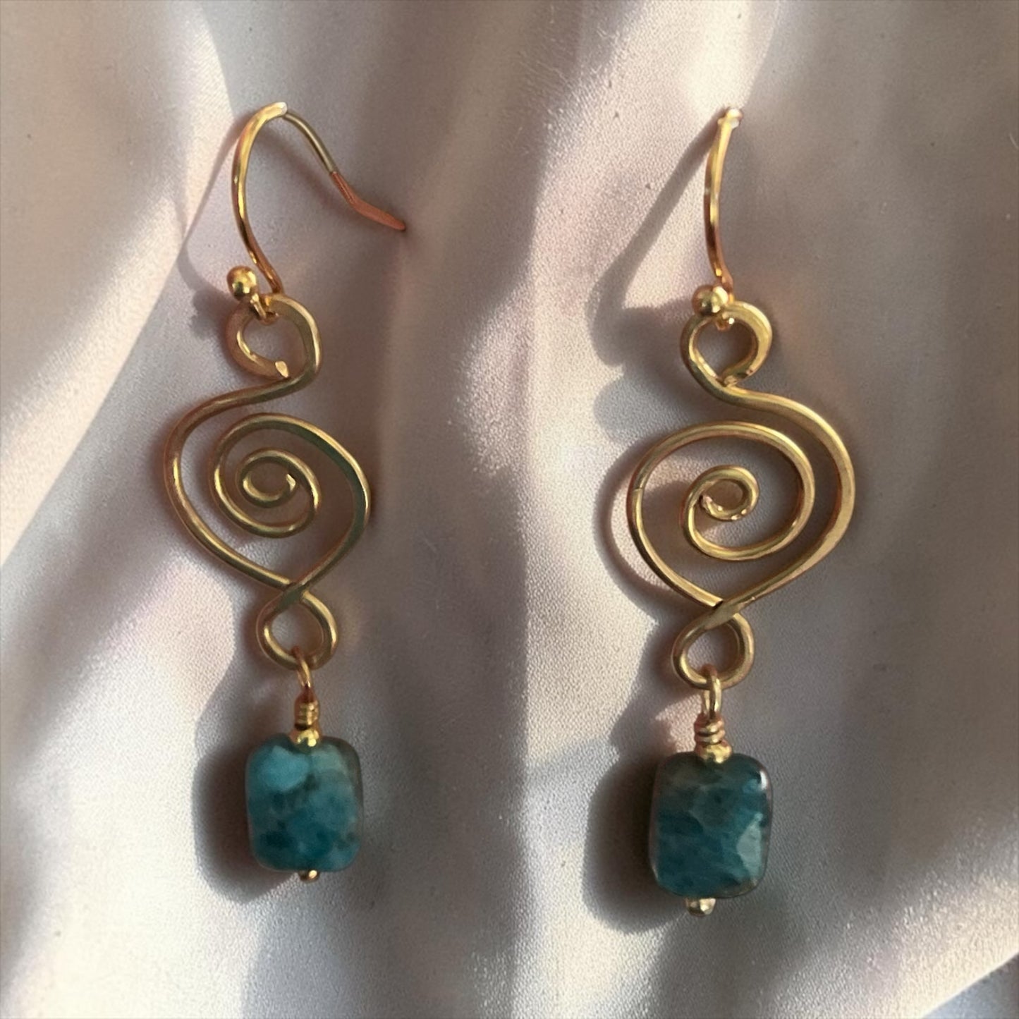 Blakeley Lane Jewelry gold-tone wire spiral drop earrings with faceted blue-green gemstone beads on silk fabric.