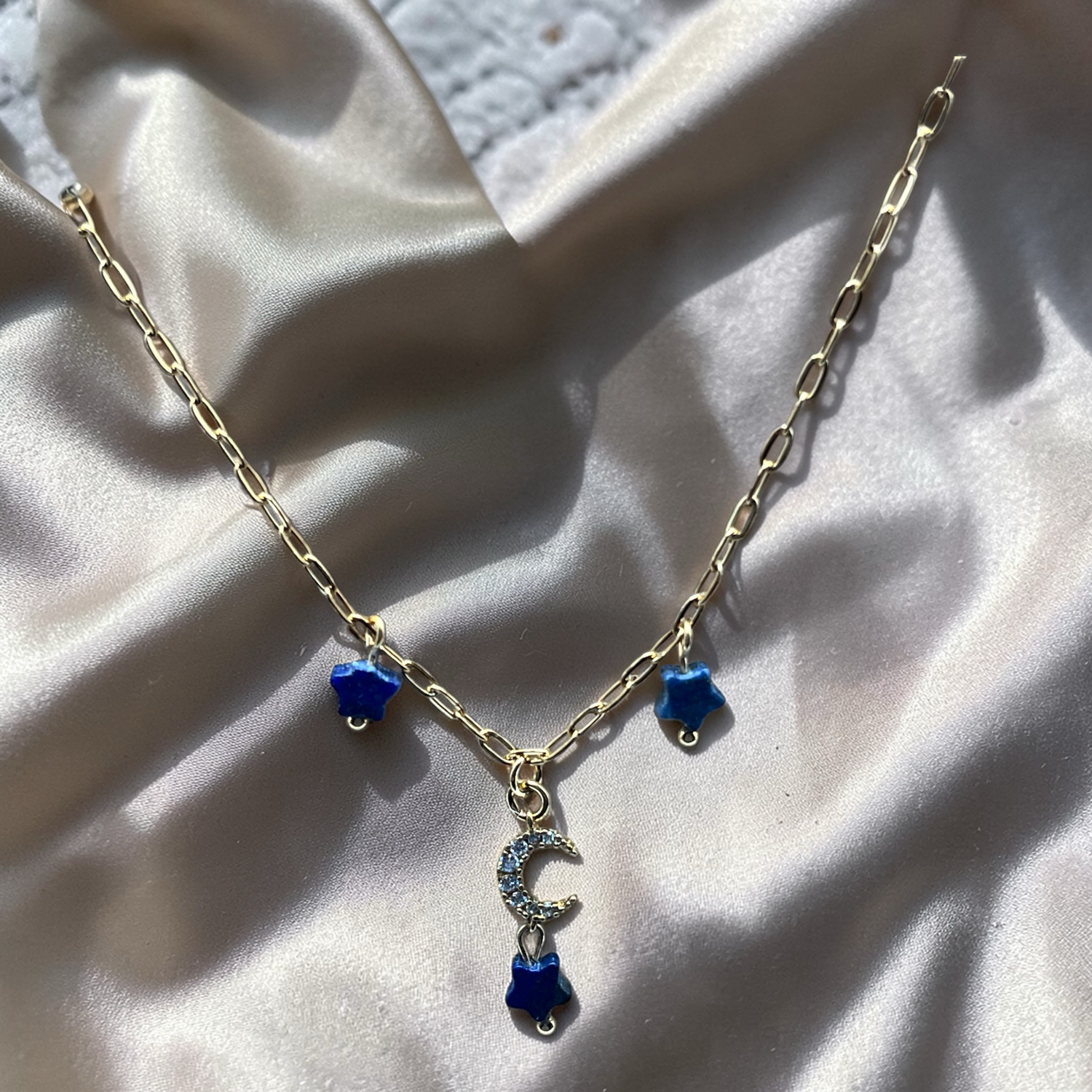 Gold necklace with blue charms on a beige fabric background