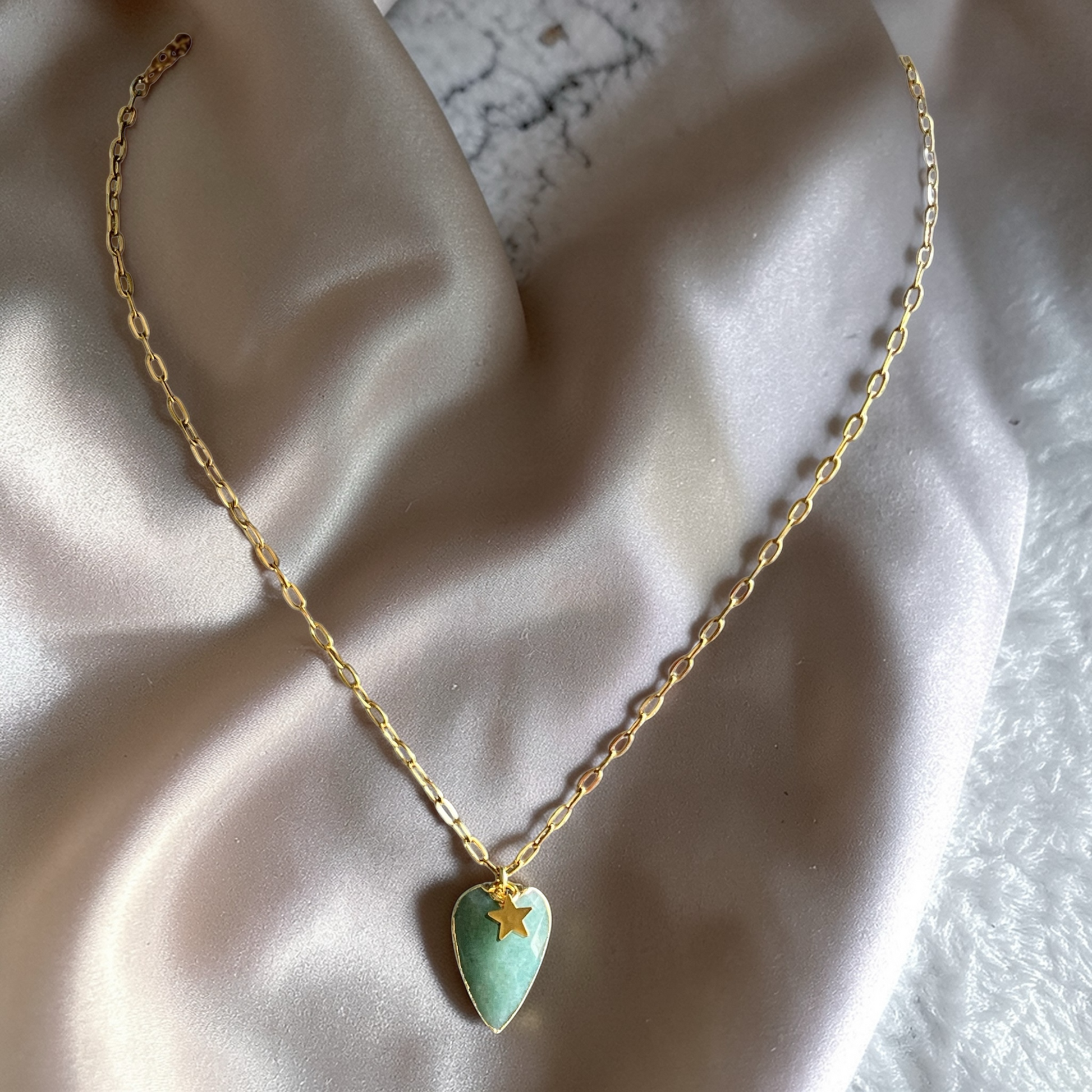 Gold necklace with a heart-shaped strawberry green  pendant and a small green star charm.
