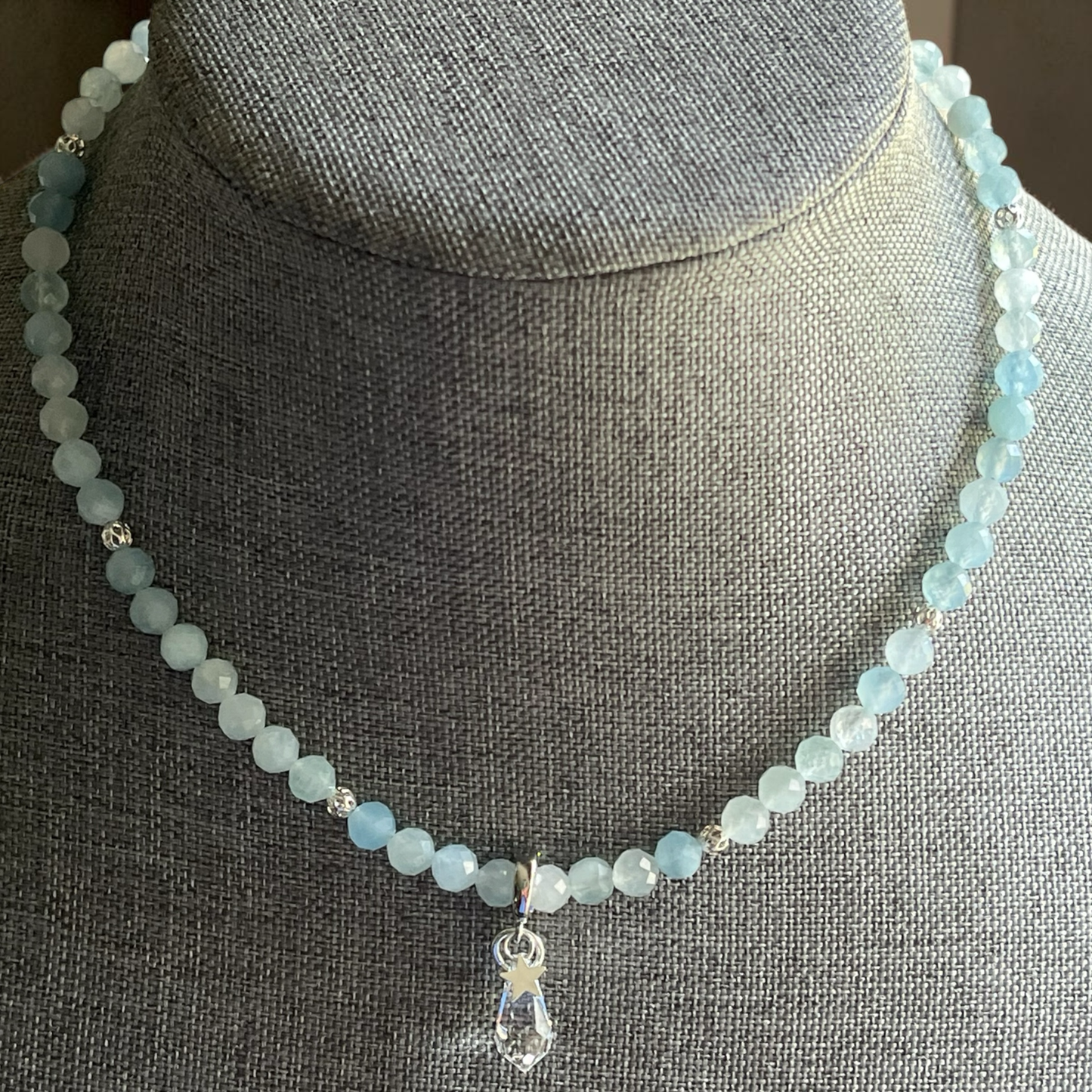 Necklace with light blue beads and a clear crystal pendant on a gray mannequin.