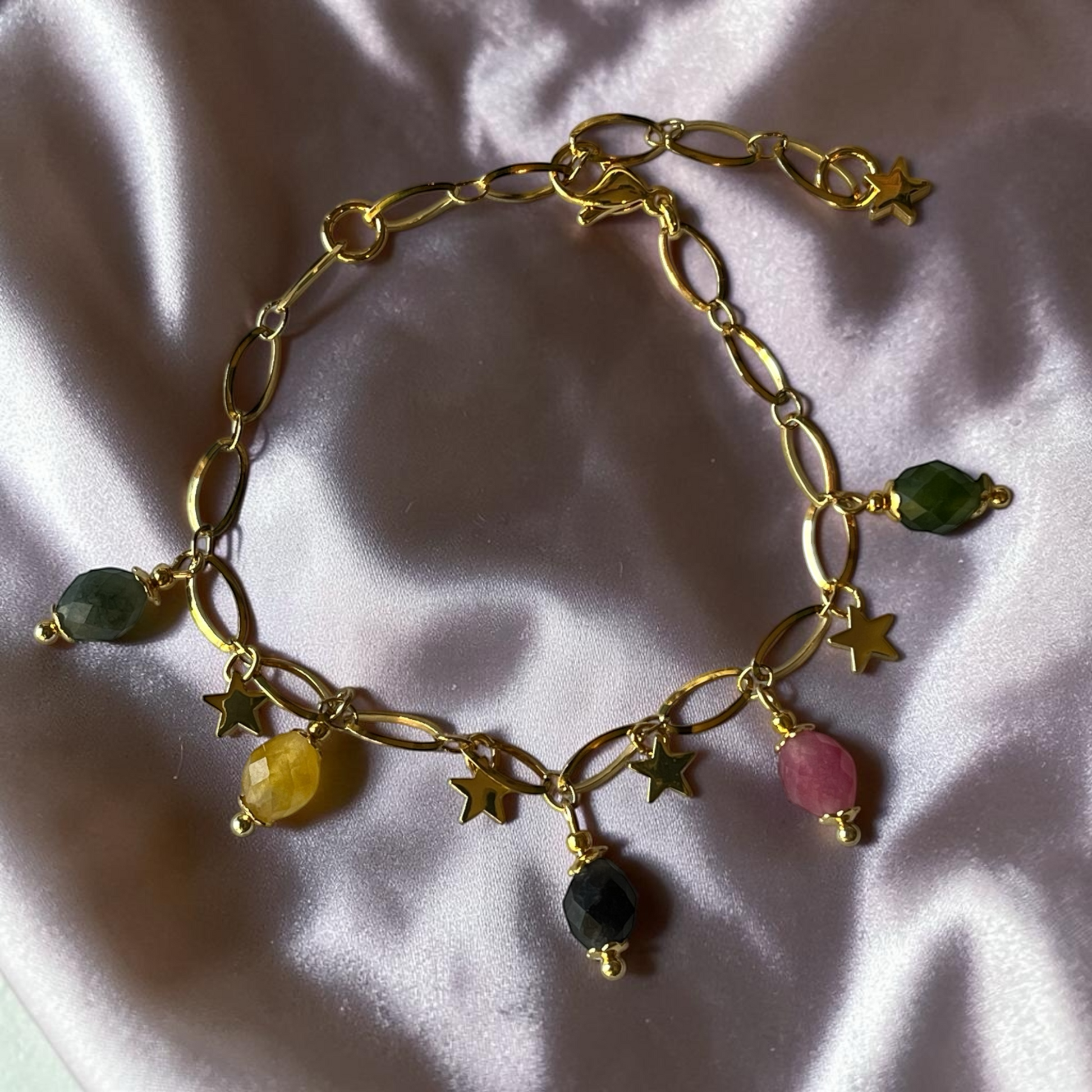 Gold bracelet with star and gemstone charms on a light pink fabric background