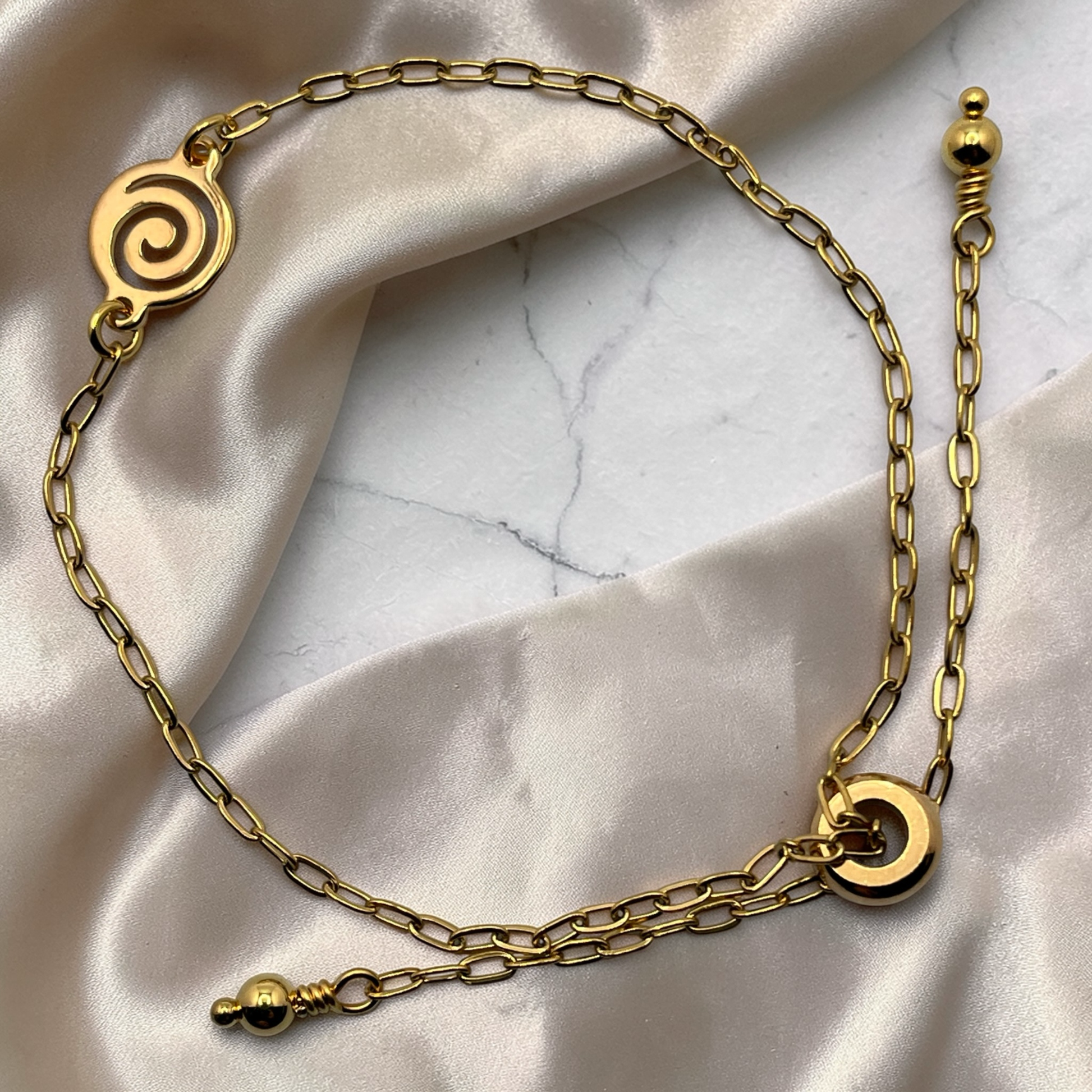 Gold chain bracelet with decorative elements on a marble surface