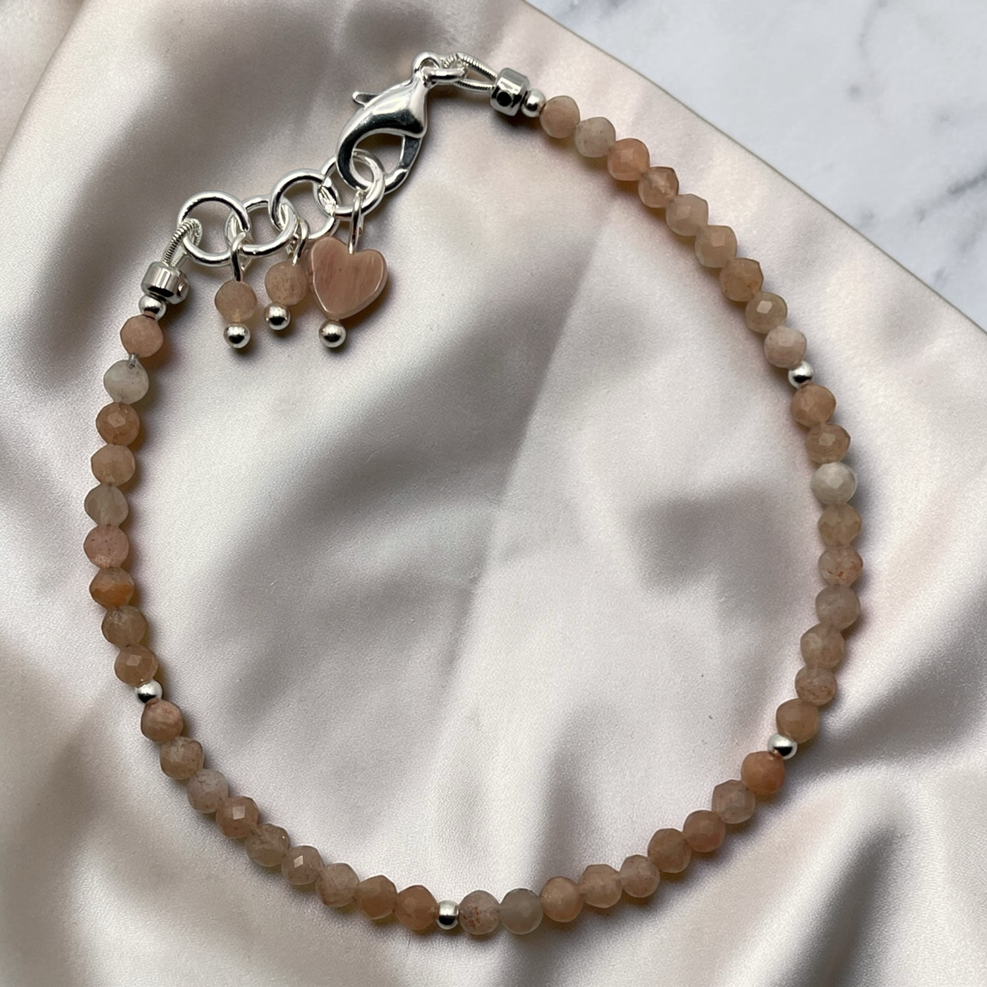 Beaded bracelet with heart charms on a soft fabric background