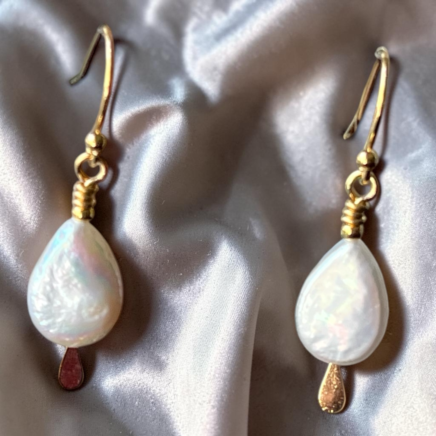 Pair of pearl earrings with gold hooks on a textured surface