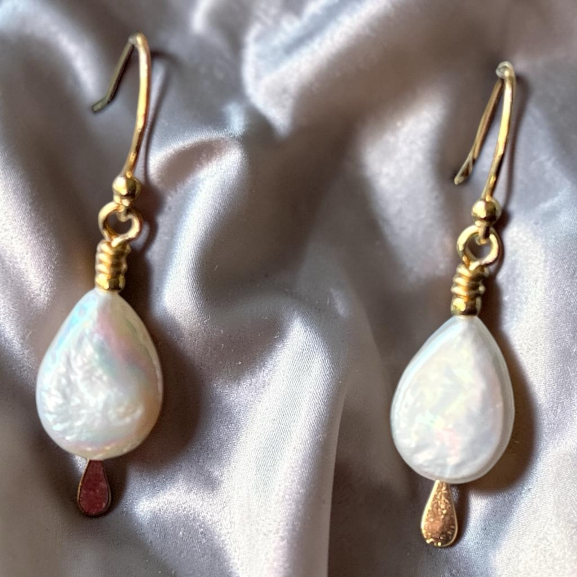 Pair of pearl earrings with gold hooks on a textured surface