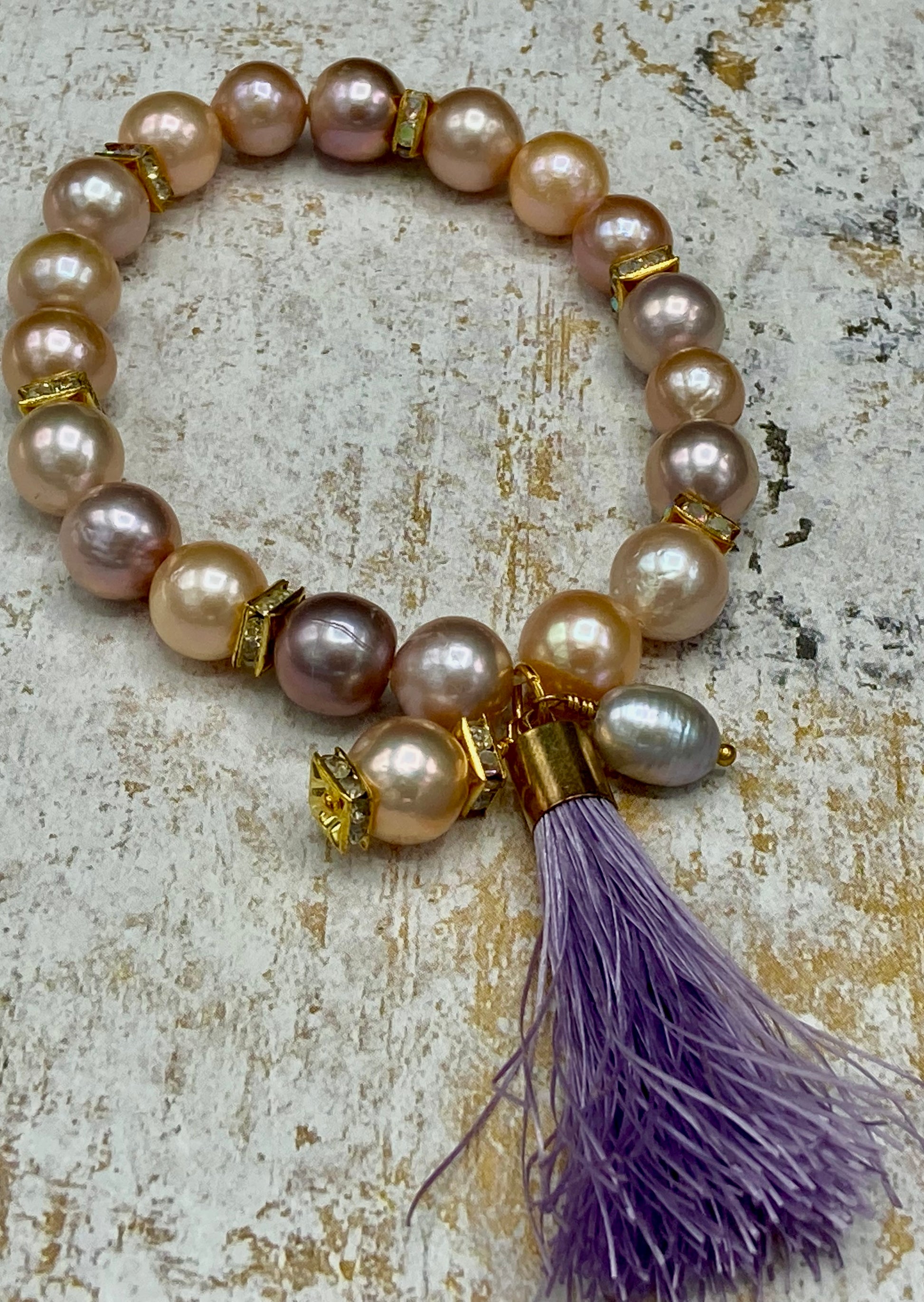 This stretch bracelet is made with pink and lavender colored pearls, and gold rondelles and is accented with a tassel and pearl dangles.