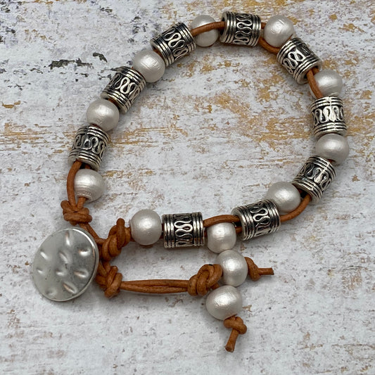 This bracelet features brown leather cording, white wood beads, and antique silver spacer beads.  It has a hammered-look metal button closure with two openings which will accommodate writs size 6.75-7.5 inches.