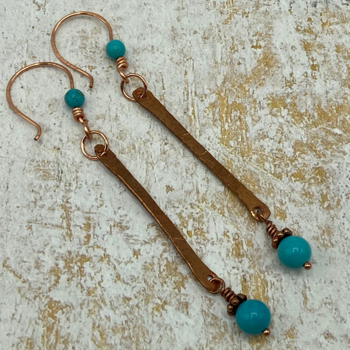 Earrings are made with copper wire that has been hammered and accented with small turquoise-colored beads. The earrings measure approximately 1.5".